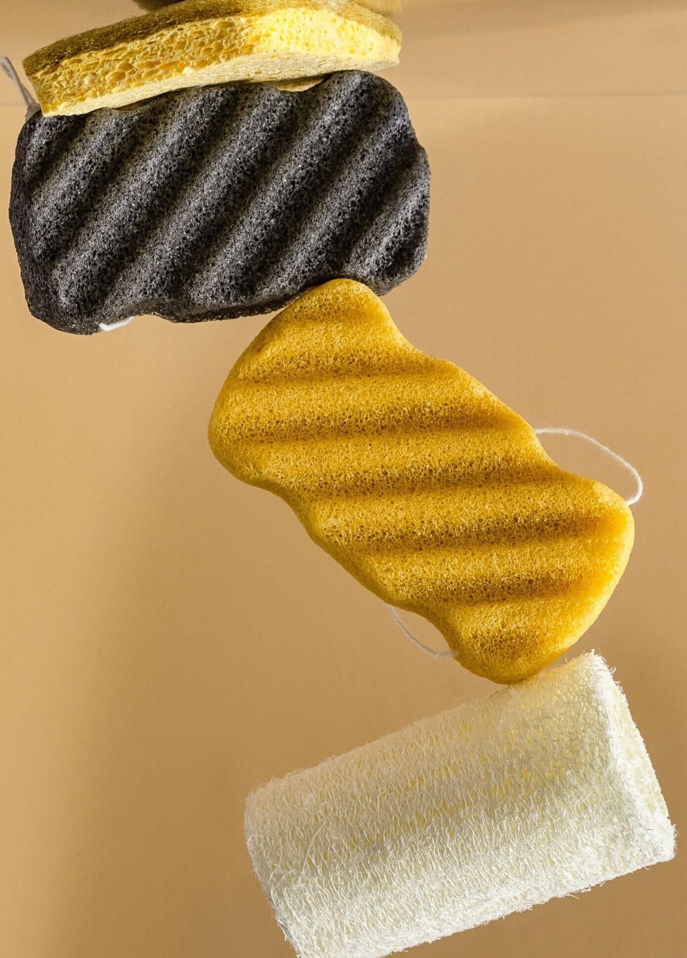 Vertical stack of colorful cleaning sponges on a neutral background.